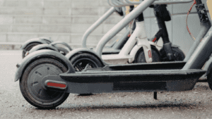 Ruedas de un patinete eléctrico aparcado vista desde ras de suelo, mostrando el suelo urbano en primer plano.