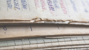 Primer plano de documentos antiguos de papel apilados, con anotaciones manuscritas y páginas desgastadas.