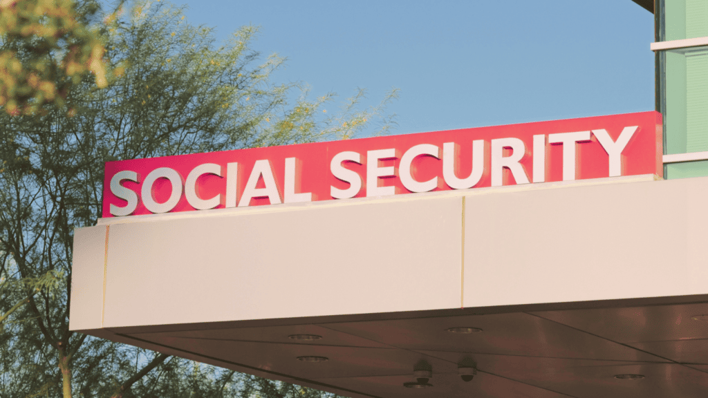 Cartel de “SOCIAL SECURITY” en la fachada de un edificio moderno, rodeado de árboles y bajo un cielo despejado.