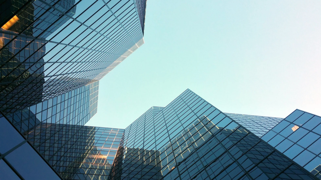 Edificios corporativos modernos con fachadas de vidrio azul reflectante vistos desde abajo bajo un cielo despejado.